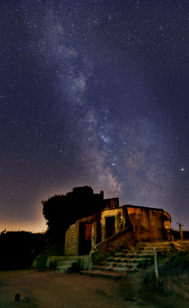 Star-filled night sky with the Milky Way above a graffitied, ruined building and steps in the foreground.
